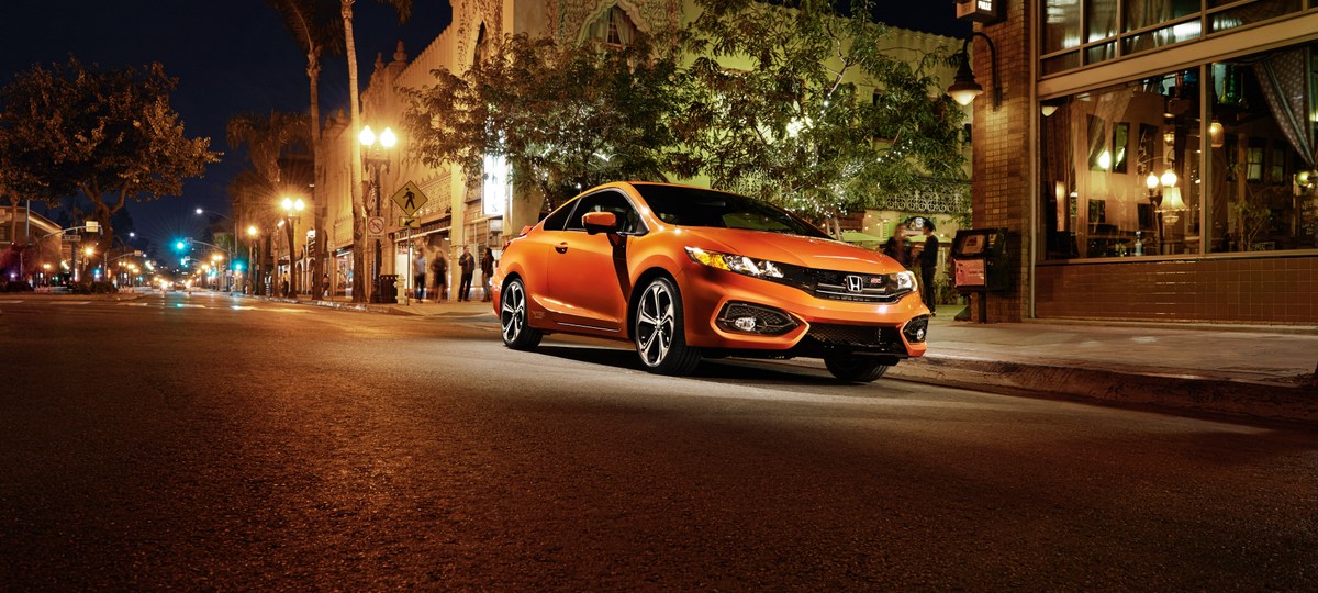 An orange 2015 Honda Civic Si Coupe parked on a city street at night.