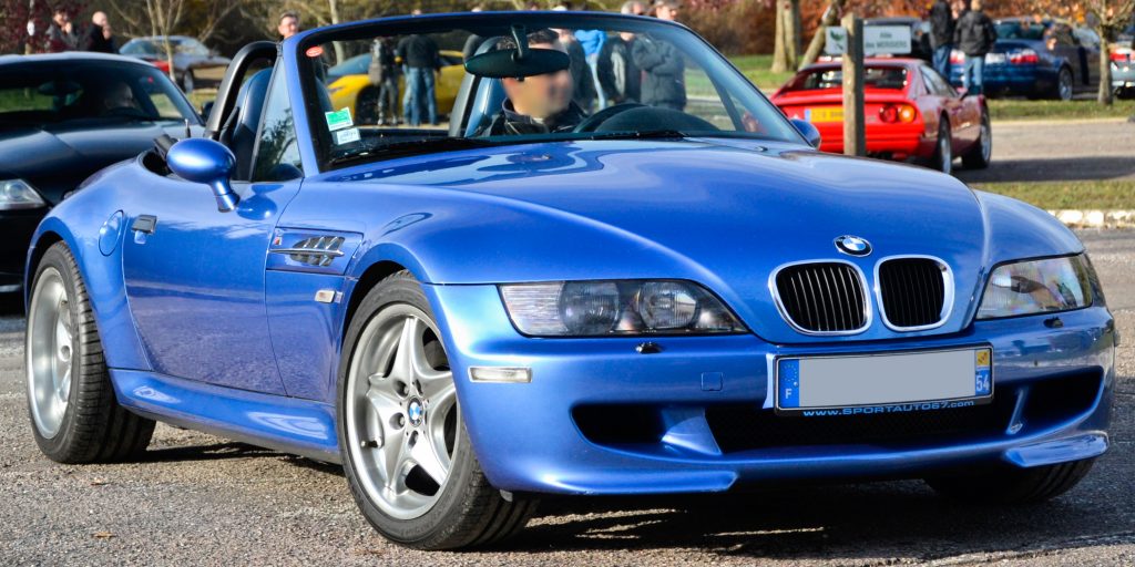A blue 1997 BMW Z3 M Roadster is parked with its convertible top down in a parking lot.