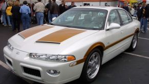A white 2001 Oldsmobile Intrigue with a tacky body kit is parked at a car show.
