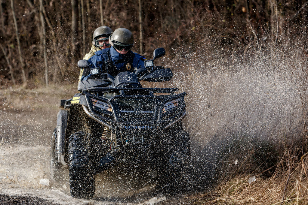 Two people drive an ATV off-road through a muddy creek.