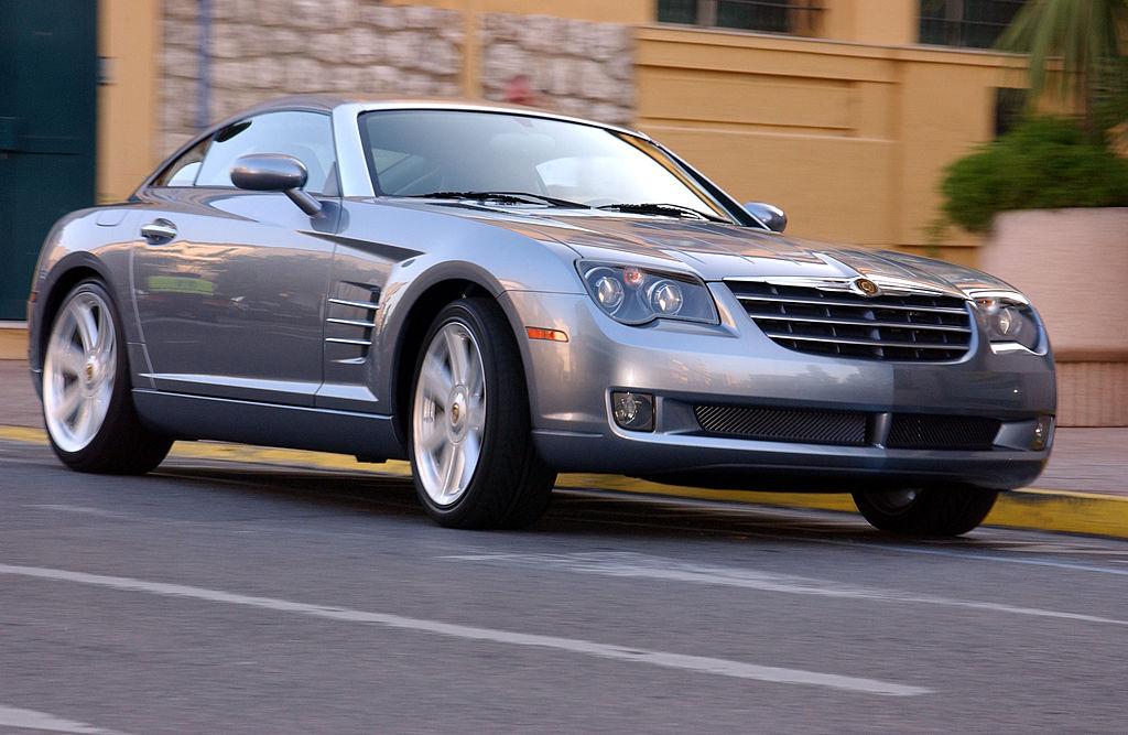 A silver 2003 Chrysler Crossfire driving quickly through a city street.