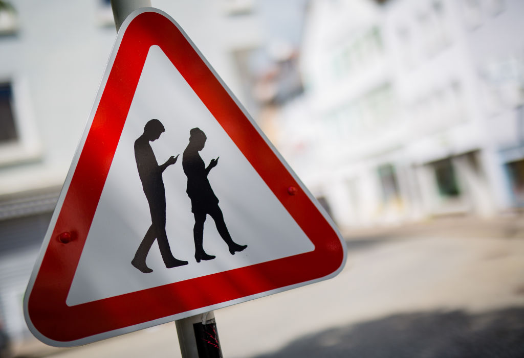 A street sign warning drivers of distracted pedestrians crossing.
