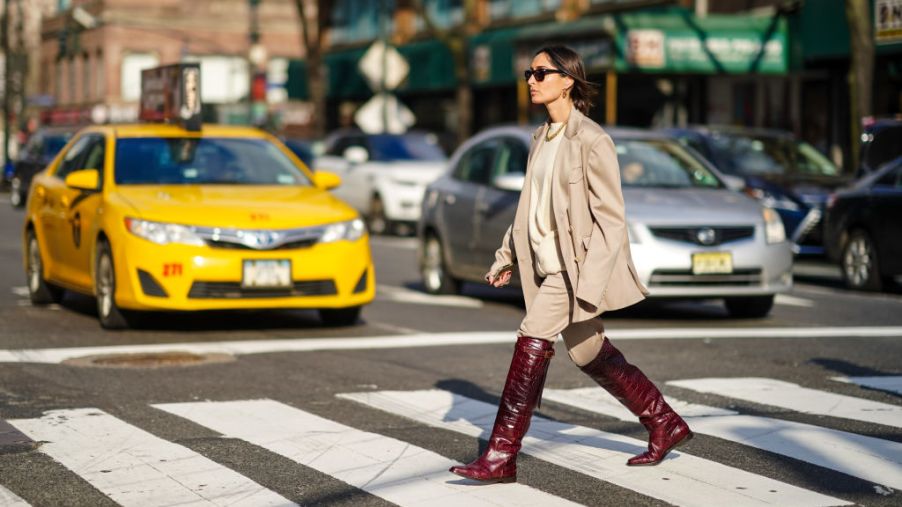 Geraldine Boublil wears sunglasses, a golden necklace, an oversized blazer jacket, a white wool pullover, beige pants, burgundy leather crocodile pattern boots, outside Sies Marjan, during New York Fashion Week Fall Winter 2020