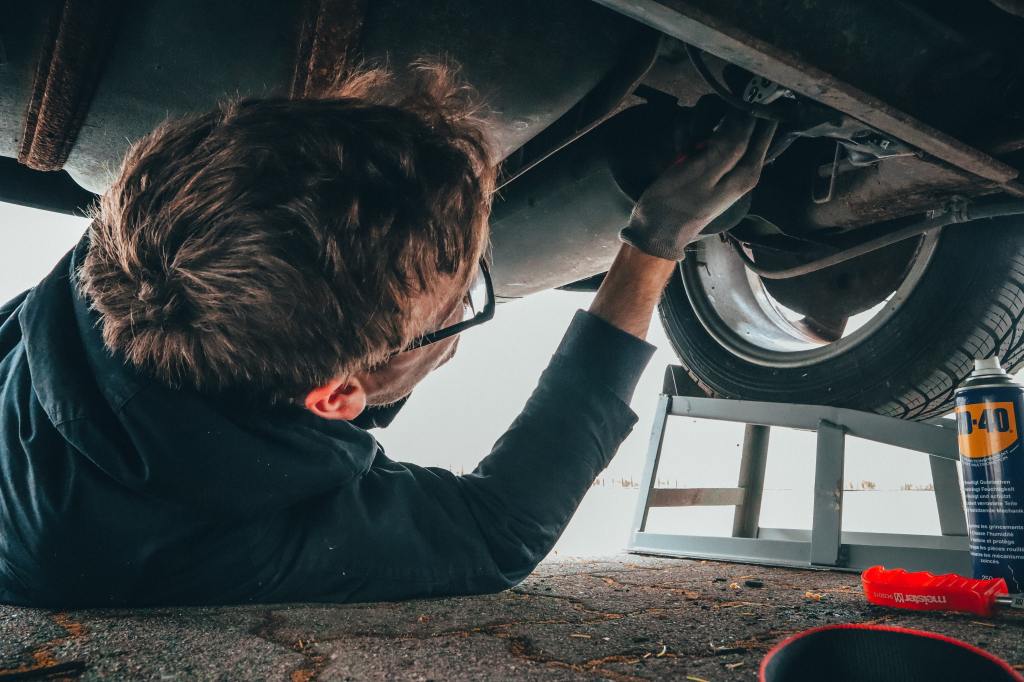 A mechanic inspects the undercarriage of a car.
