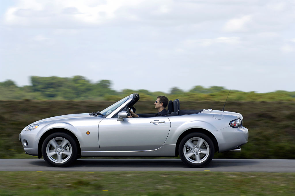 A Silver 2006 Mazda MX-5 on the road with the top down