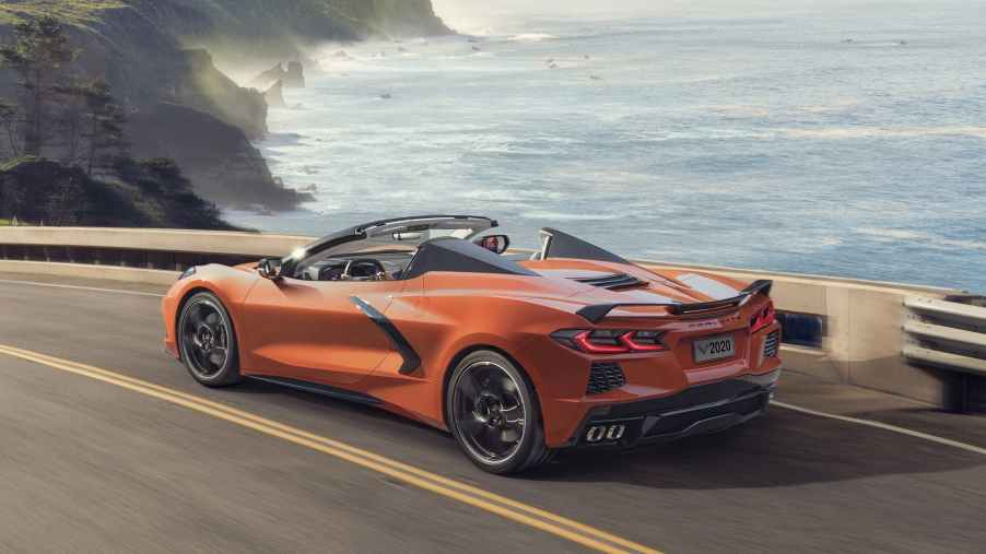 An orange Corvette is on a coastal road by cliffs
