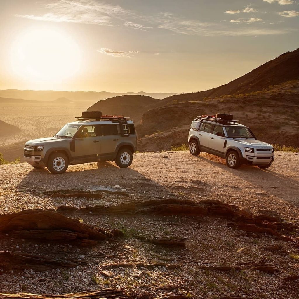 two land rover defenders in a remote desert scene with the sun giving backlighting