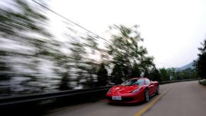 A red Ferrari 458 Italia, like the famed 2.7 GPA car, speeds down a back road.