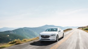 a white mazda6 at speed on a scenic road against a mountainous backdrop