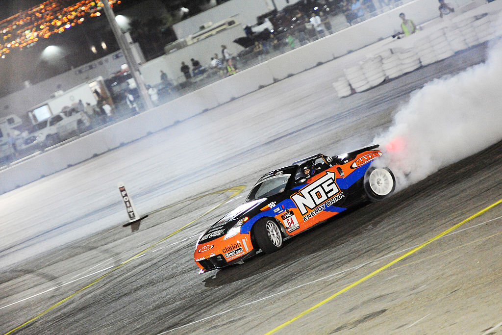 A blue and orange Nissan 350Z with a large white NOS decal drifts around a corner at the Las VEgas Motor Speedway