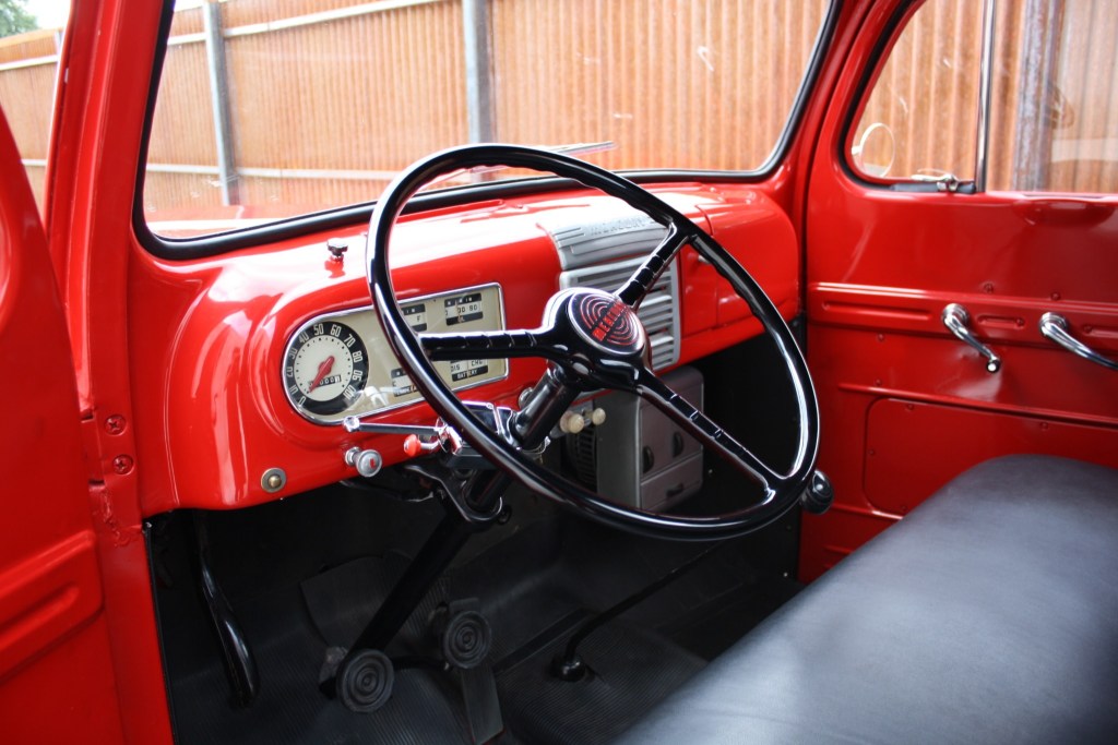 Red 1949 Mercury M47 pickup truck interior with black viny seat, red dashboard, and black 3-spoke steering wheel