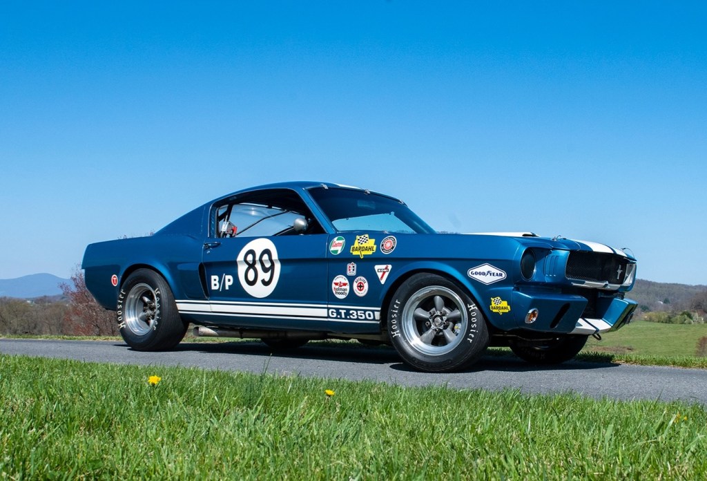 A 1965 Ford Shelby GT350 Mustang modified for racing, with blue paint, white racing stripes, and period-correct stickers