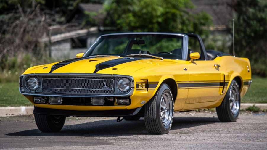 A yellow 1970 Shelby sits in the sun with its top down