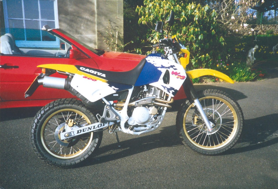 1995 Cagiva W16 600 with yellow, blue, and white livery, next to red car