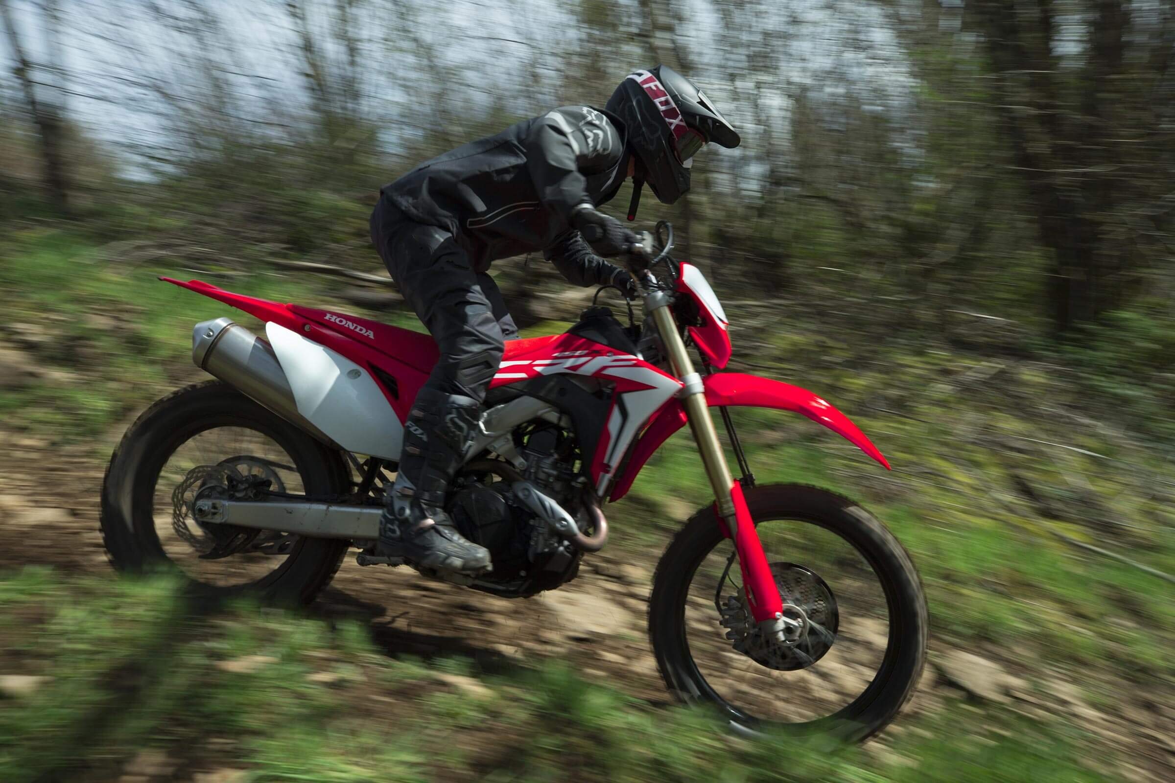 Red-and-white 2019 Honda CRF450X being ridden quickly down a forest trail