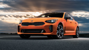 a bright orange Kia Stinger GTS parked outdoors on the road with a dreamy sky in the background