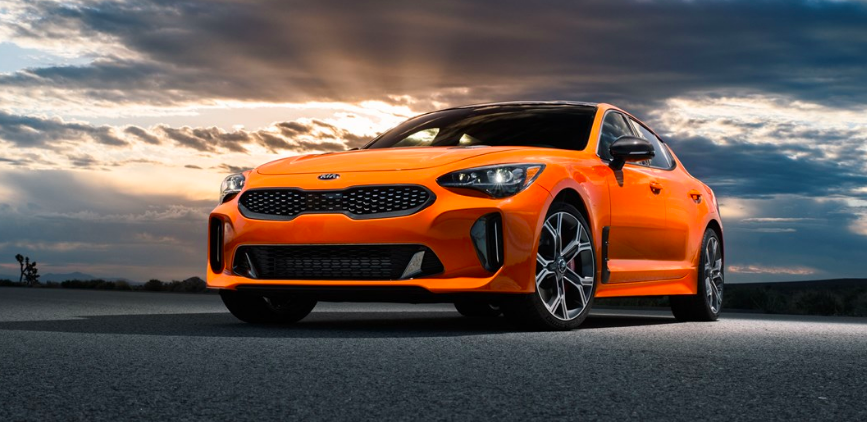 a bright orange Kia Stinger GTS parked outdoors on the road with a dreamy sky in the background