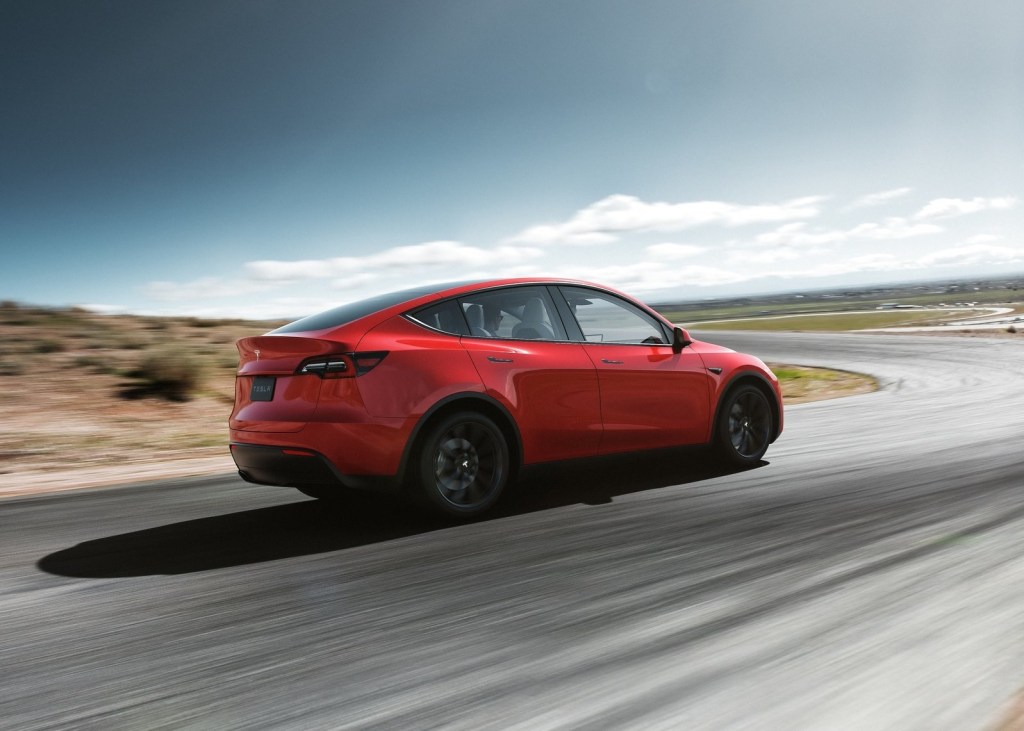 Red 2021 Tesla Model Y rear view, while it drives on a curvy road