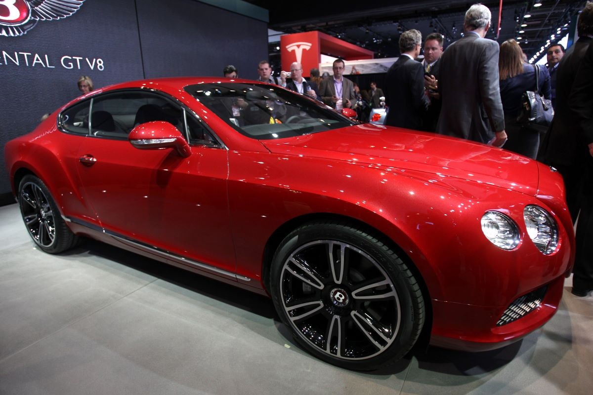 A red Bentley Continental GT sits on stage at a car show