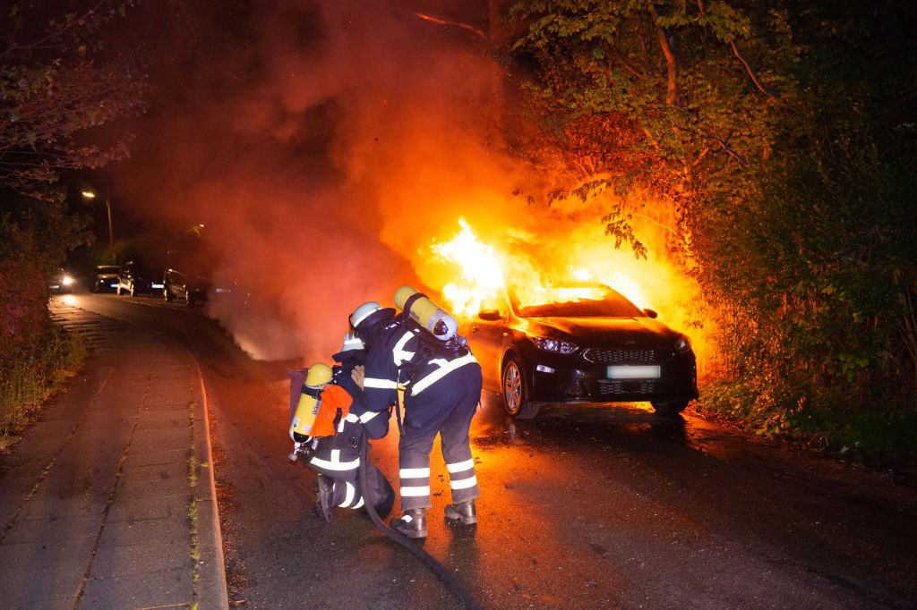 car on fire with firemen dousing flames