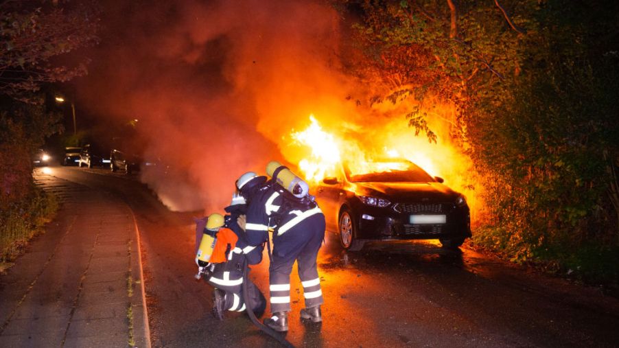 car on fire with firemen dousing flames
