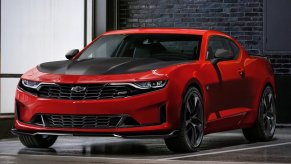 A red Camaro with black racing stripes parked on pristine concrete flooring.