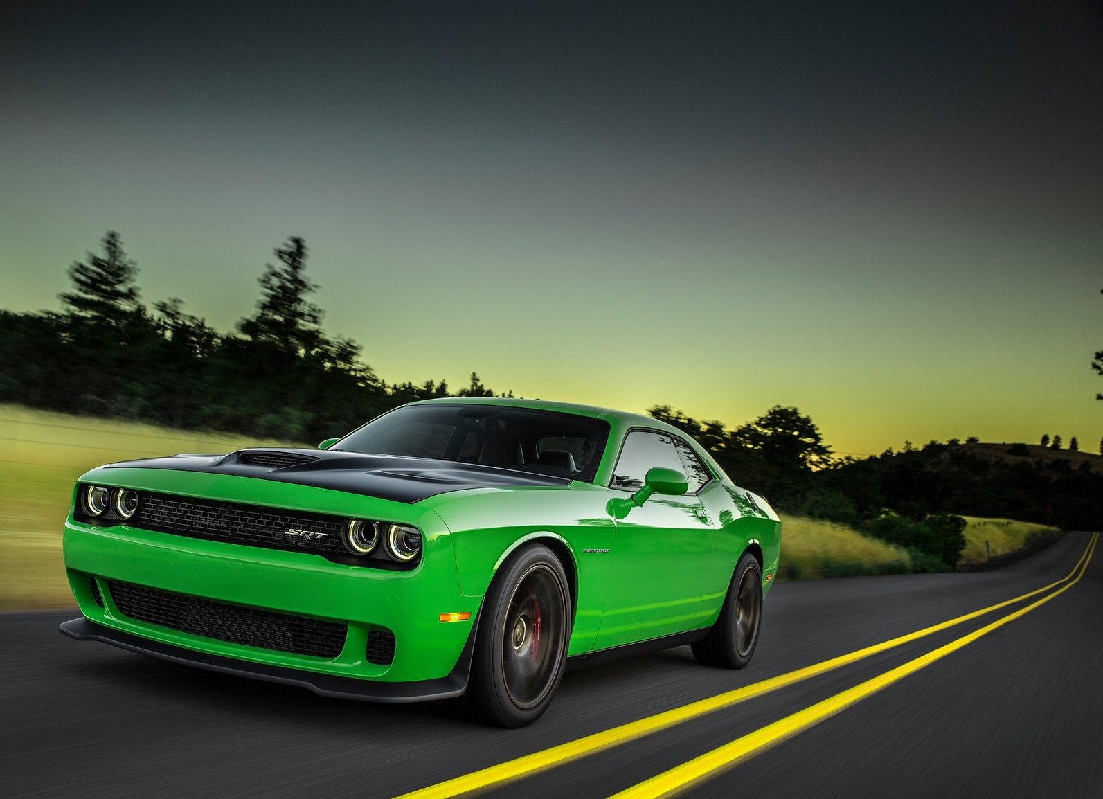 a bright green Dodge Challenger muscle car driving down a scene road at dusk