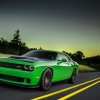 a bright green Dodge Challenger muscle car driving down a scene road at dusk