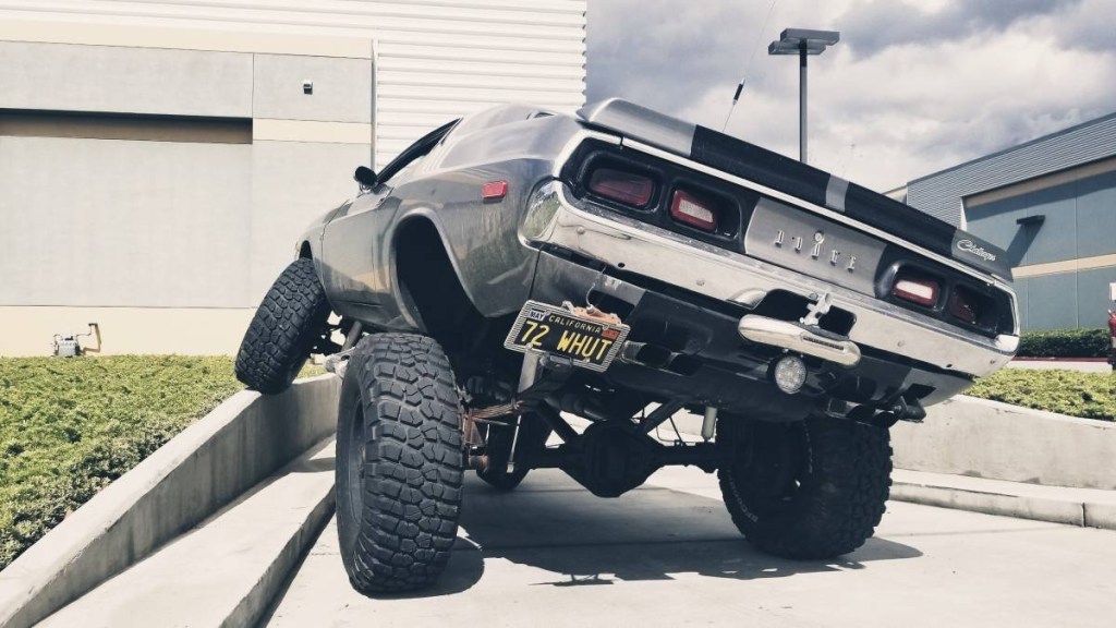 Lifted 1973 Dodge Challenger 4x4 rear view, as its front driver's wheel articulates over a concrete berm