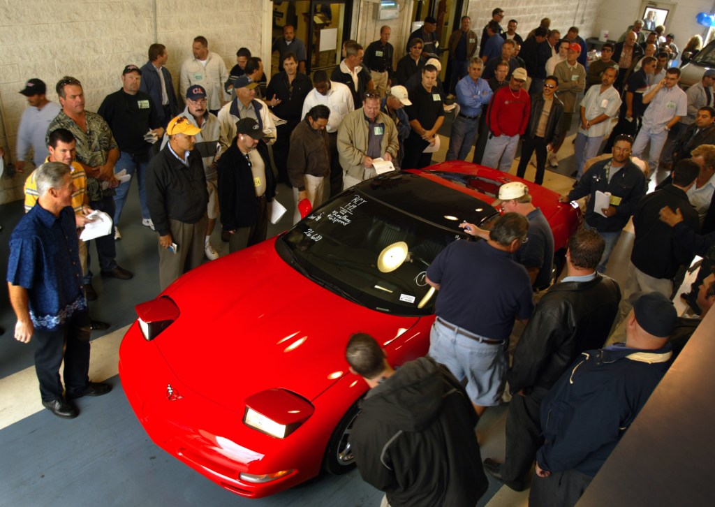 A red Corvette surrounded by dealers at a Manheim auction in California