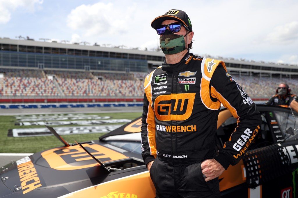 Driver Kurt Busch stands by his NASCAR racecar while wearing a facemask