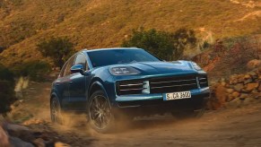 A blue Porsche Cayenne midsize SUV is driving off-road.