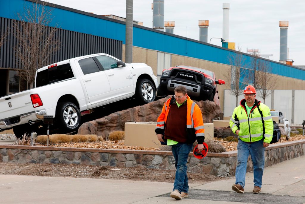 Workers leaving a factory with two Ram 1500 trucks in the background