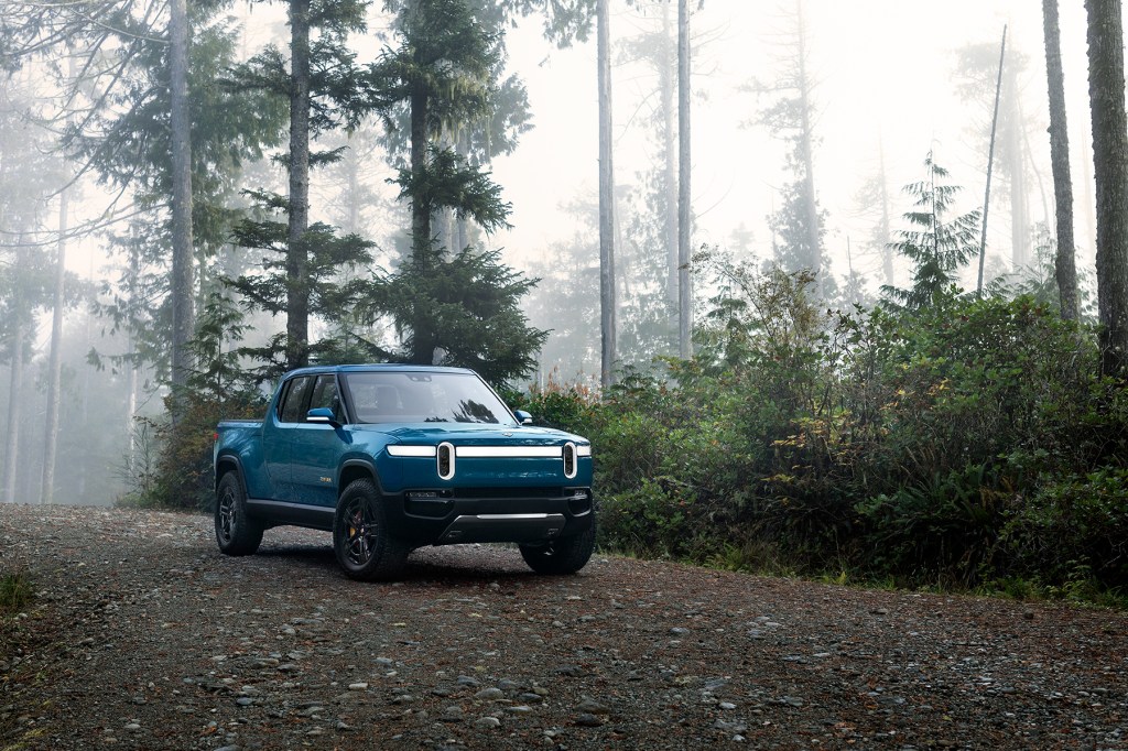 A blue Rivian R1T pickup on a forest road