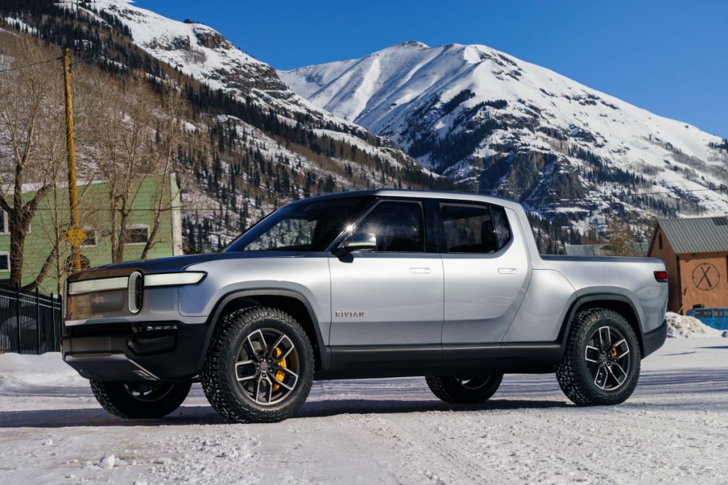A silver Rivian R1T pickup sits at the base of snow-capped mountains