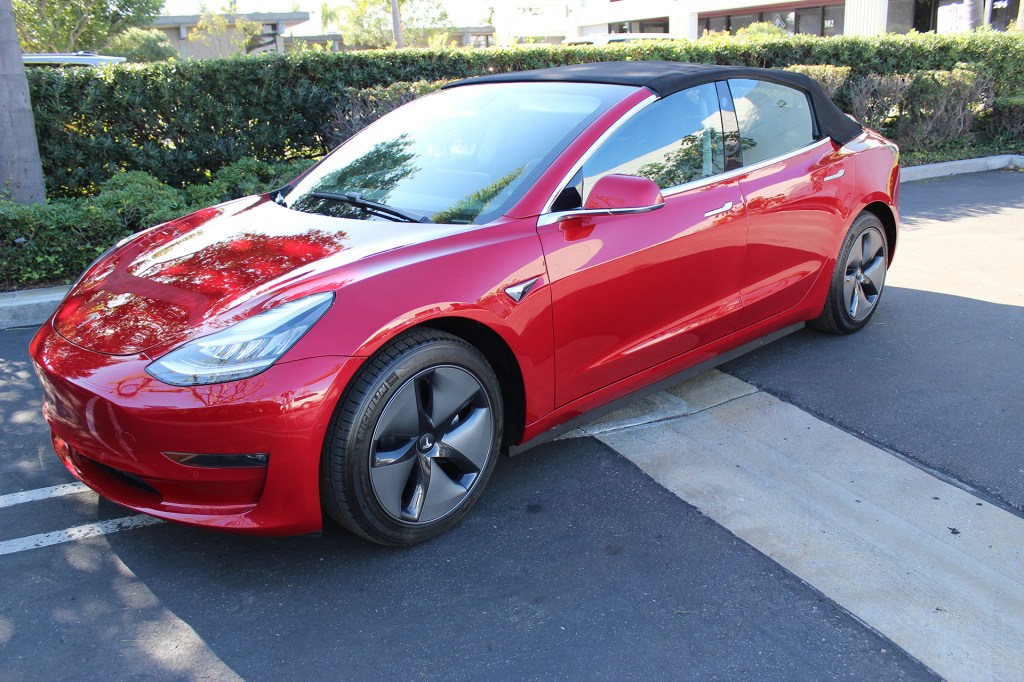 A red Tesla Model 3 convertible with its soft top up