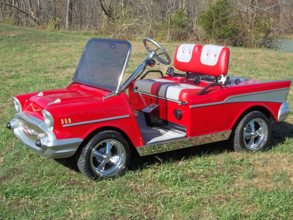 A red 1957 Chevy bodied golf cart sits in a yard