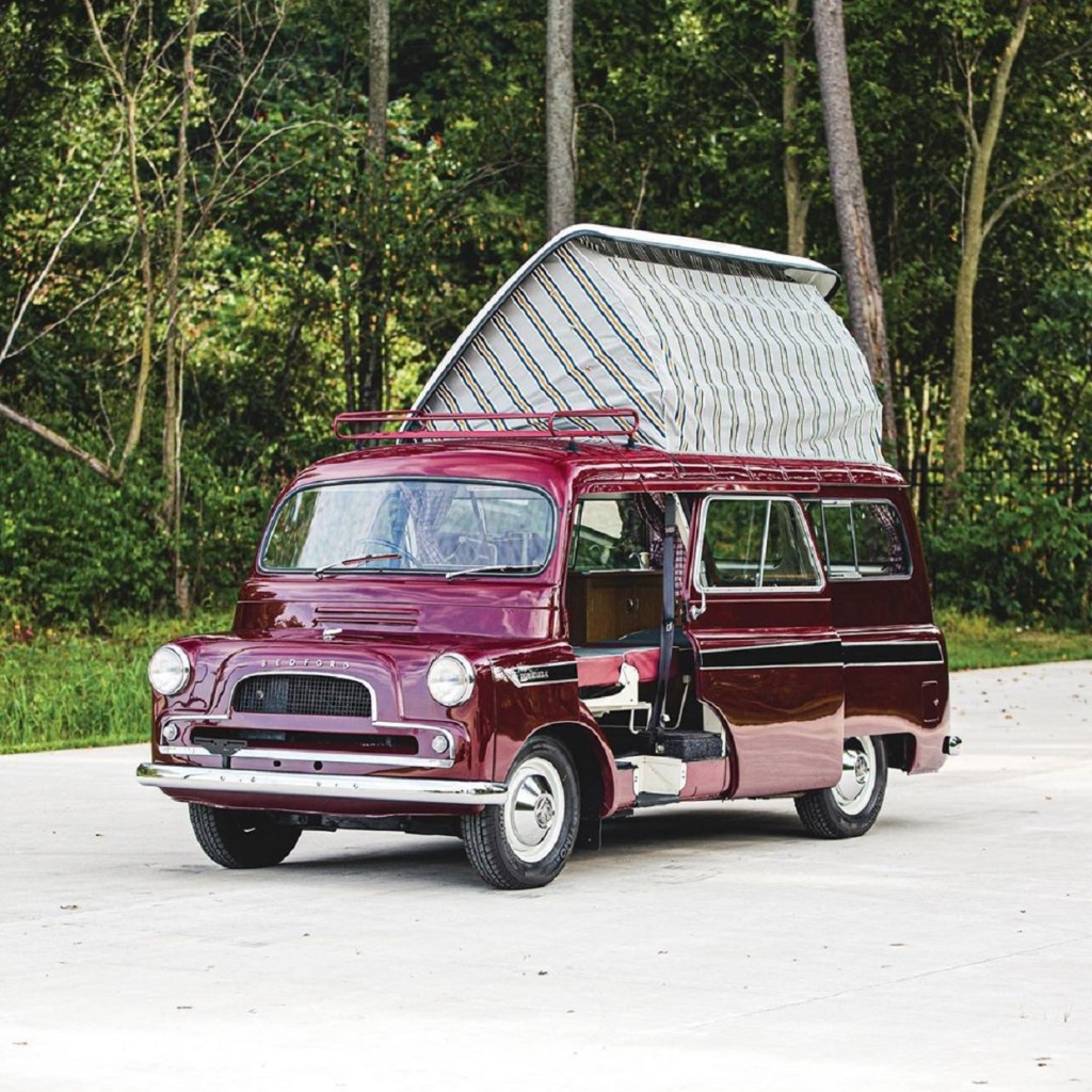 Maroon 1961 Bedford CA Dormobile camper van with its pop-up roof open in front of a forest