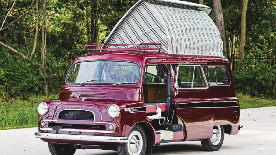 Maroon 1961 Bedford CA Dormobile camper van with its pop-up roof open in front of a forest