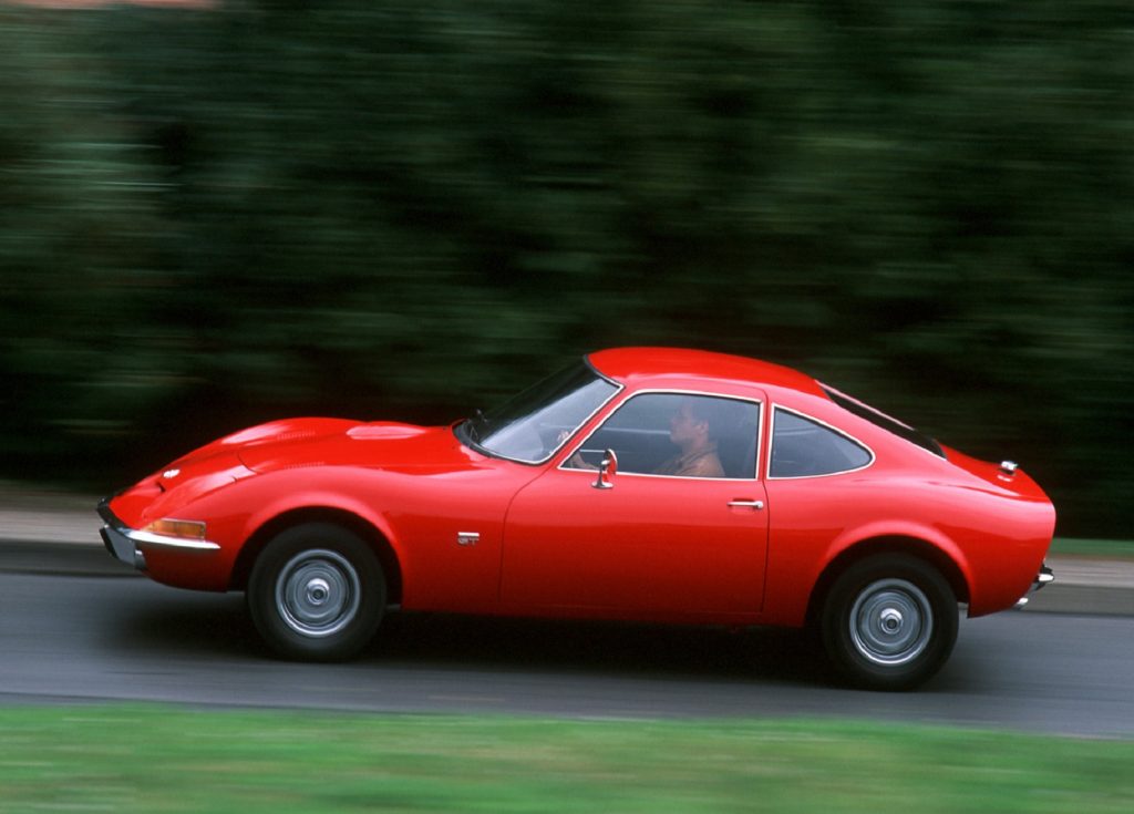 Red 1968 Opel GT, driving down the road, side view