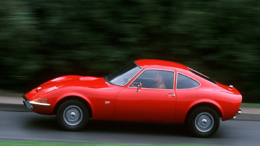 Red 1968 Opel GT, driving down the road, side view