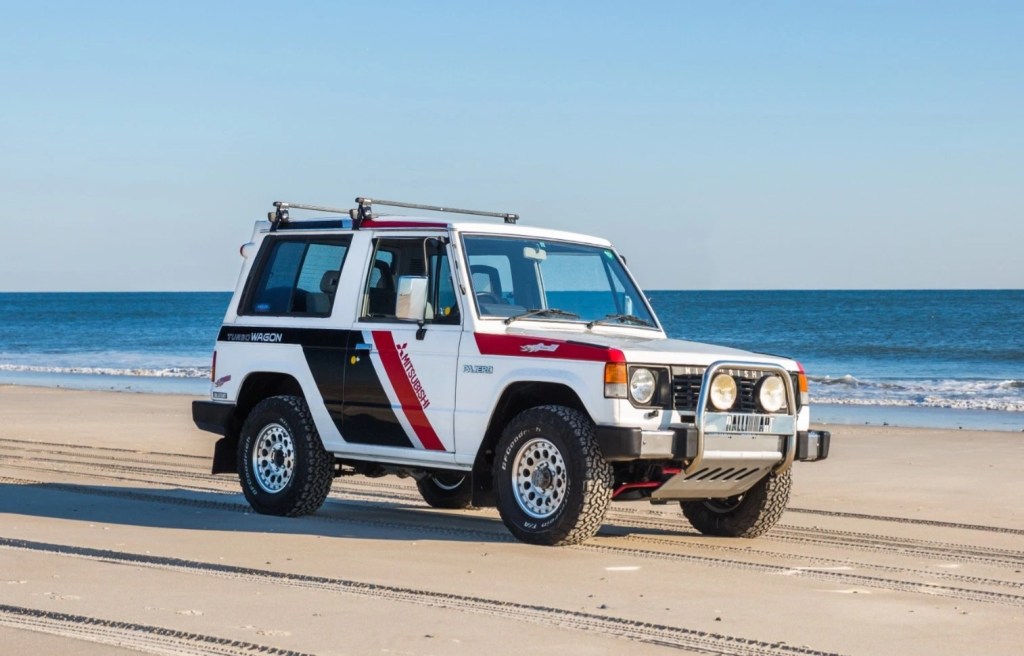 The white-with-black-and-red-stripes 1988 Mitsubishi Pajero Paris-Dakar Special classic SUV driving down the beach