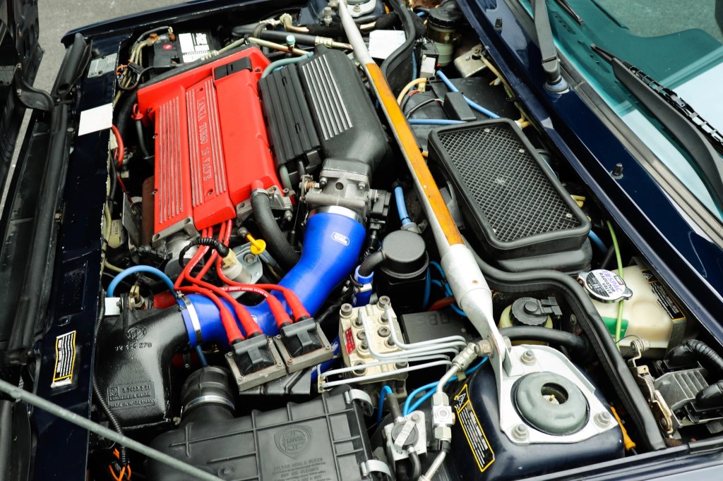 The engine bay of a dark blue 1994 Lancia Delta Integrale Evoluzione II, showing the red engine cover and the suspension towers rising up to the edge of the engine bay