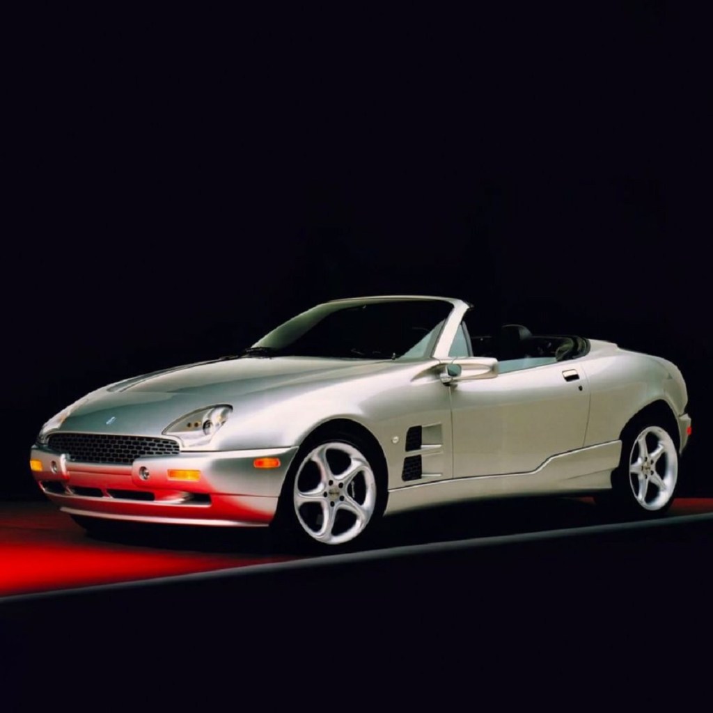 Silver 1999 Qvale Mangusta with the roof down against a black background