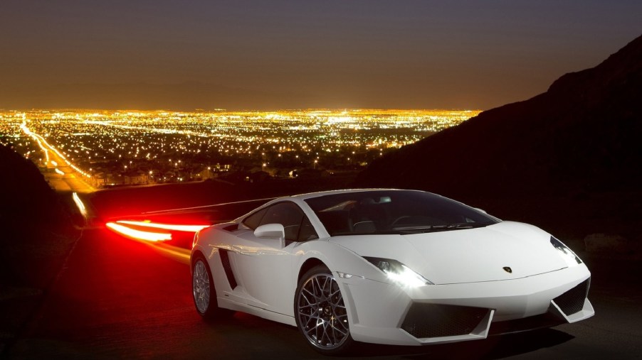 White 2009 Lamborghini Gallardo LP560-4 on a mountain road overlooking a bright-lit city at night