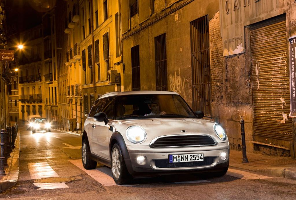 A white Mini Clubman drives down an urban street at night