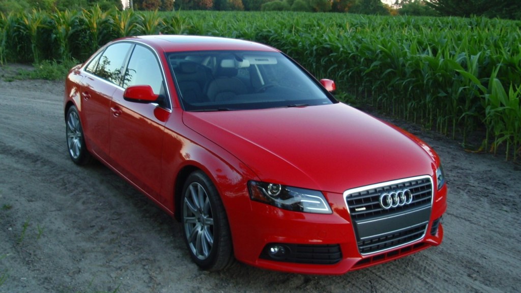 A red Audi sedan sits on a road by hedges