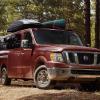 a dark red Nissan NV driving off road in the forest with recreational gear loaded up top