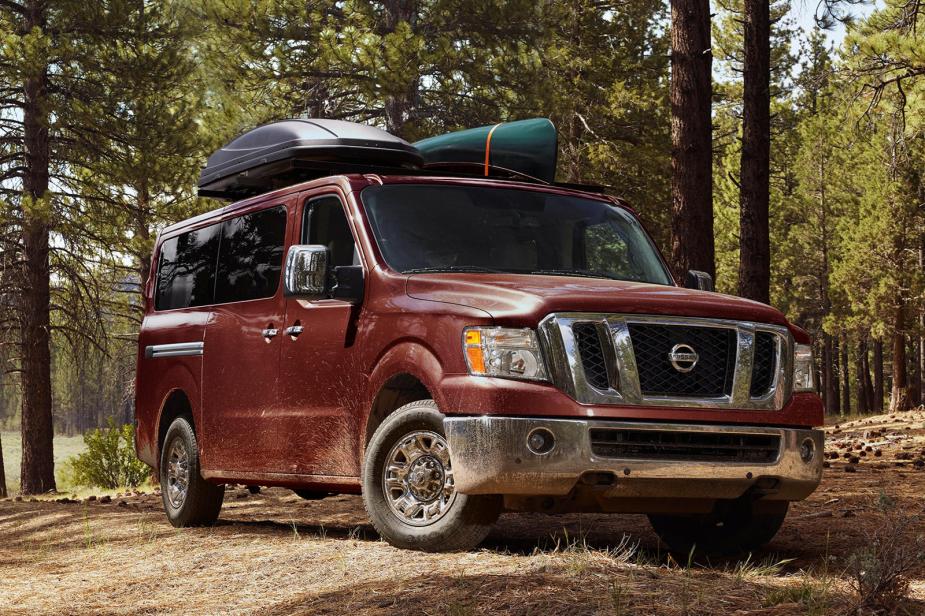 a dark red Nissan NV driving off road in the forest with recreational gear loaded up top