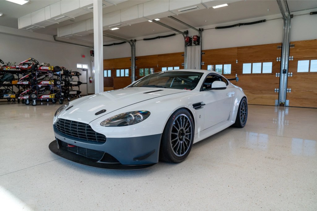White 2013 Aston Martin V8 Vantage GT4 with blue bumper sitting in garage